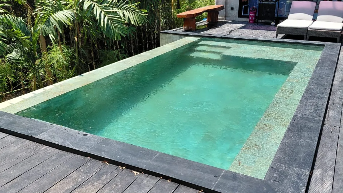 Private infinity-edge style villa pool in Bali with black stone coping, timber deck, and jungle backdrop, example of a mid-range skimmer pool build